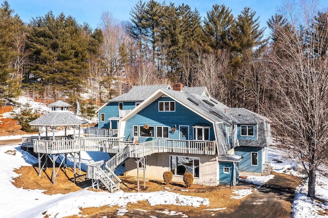 snow covered rear of property with a gazebo, a wooden deck, a chimney, and stairs