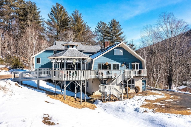 snow covered rear of property featuring a gazebo, stairway, a deck, and roof with shingles