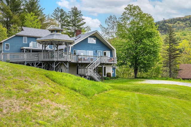 back of property with a lawn, a deck, stairs, a gazebo, and a chimney
