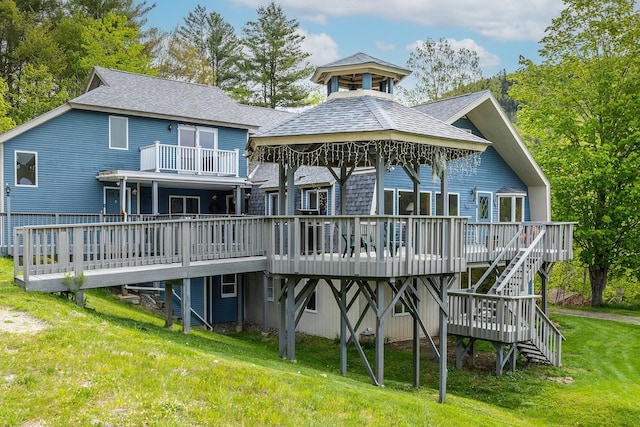 rear view of property with a wooden deck, stairway, a lawn, and a shingled roof
