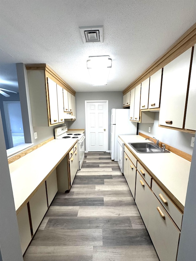 kitchen featuring under cabinet range hood, light countertops, wood finished floors, white appliances, and a sink