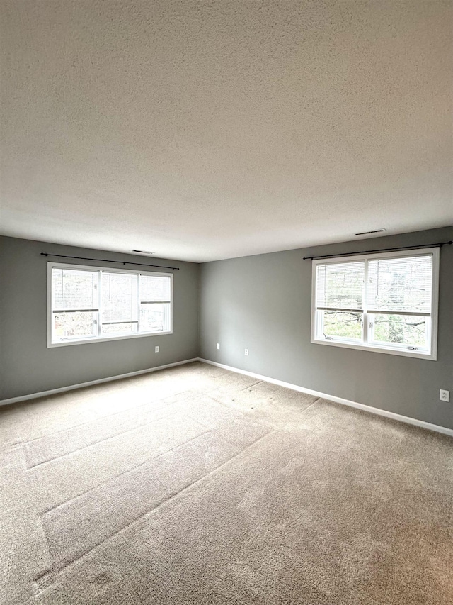 carpeted empty room featuring a textured ceiling and baseboards