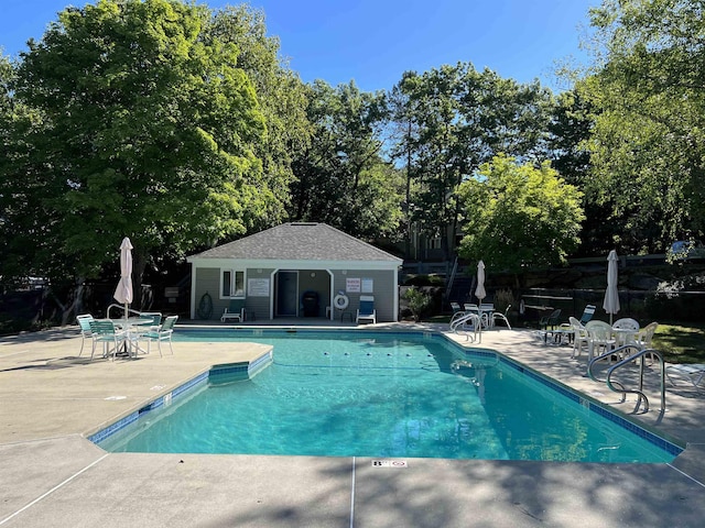 pool featuring a patio, fence, and an outbuilding