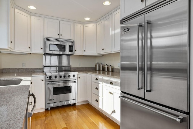 kitchen with white cabinets, recessed lighting, premium appliances, and light wood-type flooring