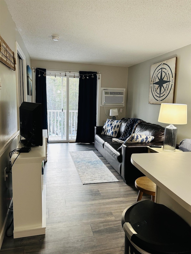 living room featuring a wall mounted air conditioner, a textured ceiling, and wood finished floors