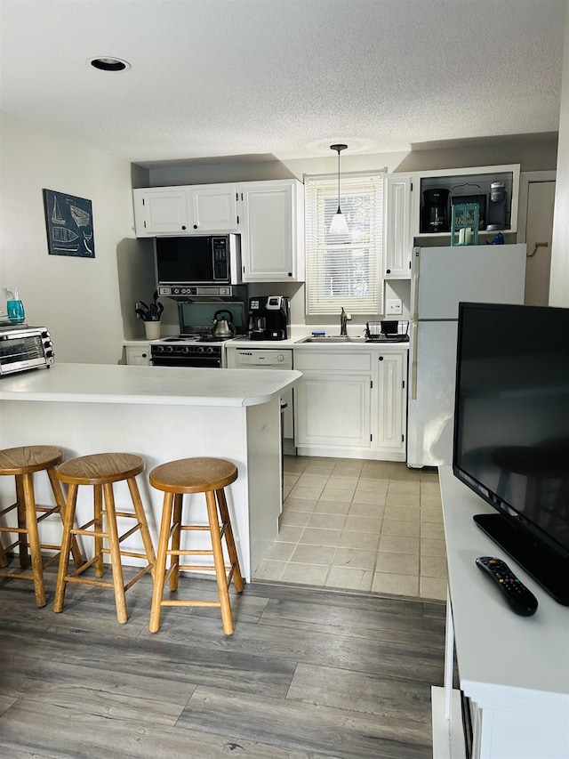 kitchen featuring white stove, white cabinets, light countertops, a sink, and a breakfast bar area