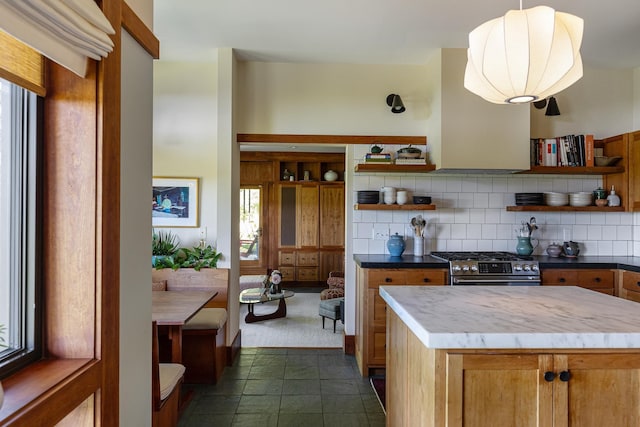 kitchen with brown cabinetry, stainless steel range with gas cooktop, open shelves, pendant lighting, and tasteful backsplash