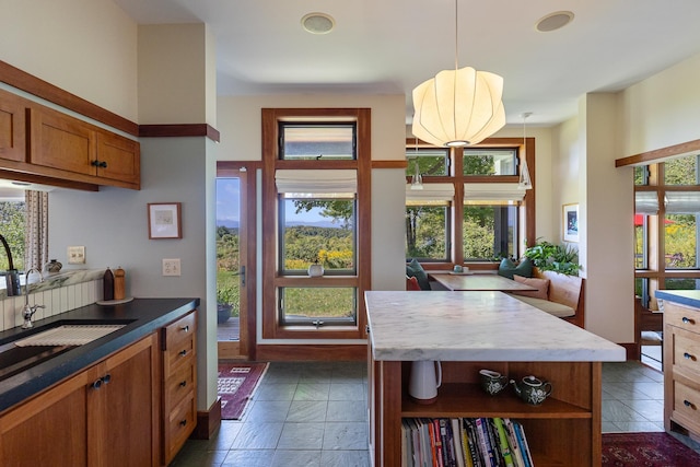 kitchen with brown cabinetry, open shelves, a sink, pendant lighting, and a center island