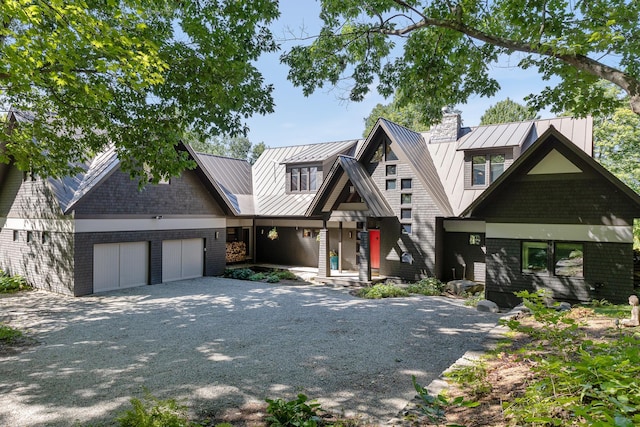 view of front of property with a standing seam roof, gravel driveway, an attached garage, brick siding, and metal roof