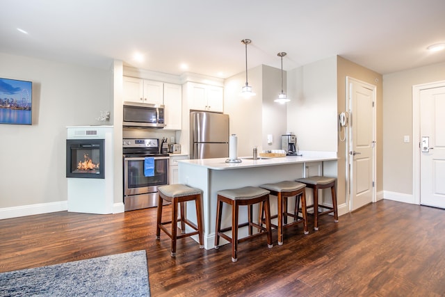 kitchen with a breakfast bar, a peninsula, stainless steel appliances, and dark wood-type flooring