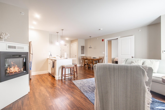 living area featuring visible vents, baseboards, a glass covered fireplace, and dark wood-style flooring