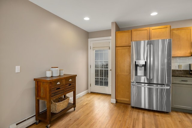 kitchen with baseboard heating, stainless steel fridge, light wood finished floors, baseboards, and backsplash