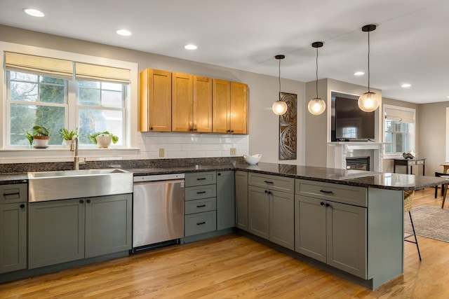 kitchen with dishwasher, a sink, a peninsula, a kitchen bar, and light wood-style flooring