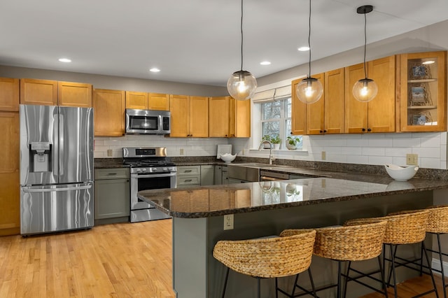 kitchen featuring dark stone countertops, tasteful backsplash, a sink, appliances with stainless steel finishes, and a peninsula