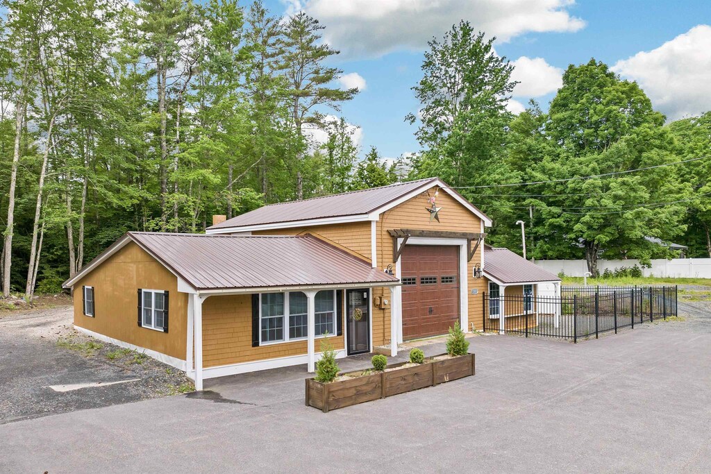view of front of house featuring driveway, metal roof, a garage, and fence