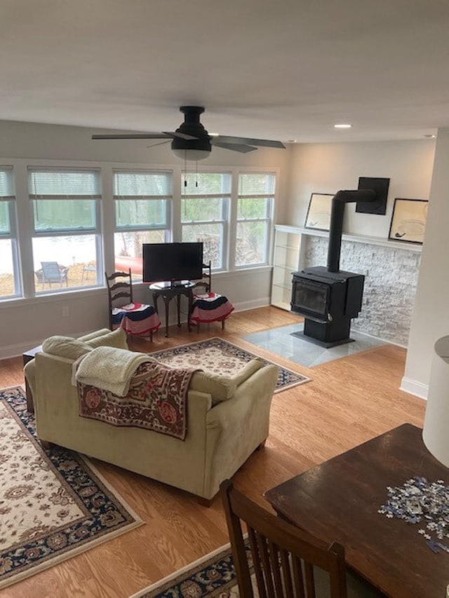 living room with a ceiling fan, wood finished floors, a wood stove, baseboards, and recessed lighting