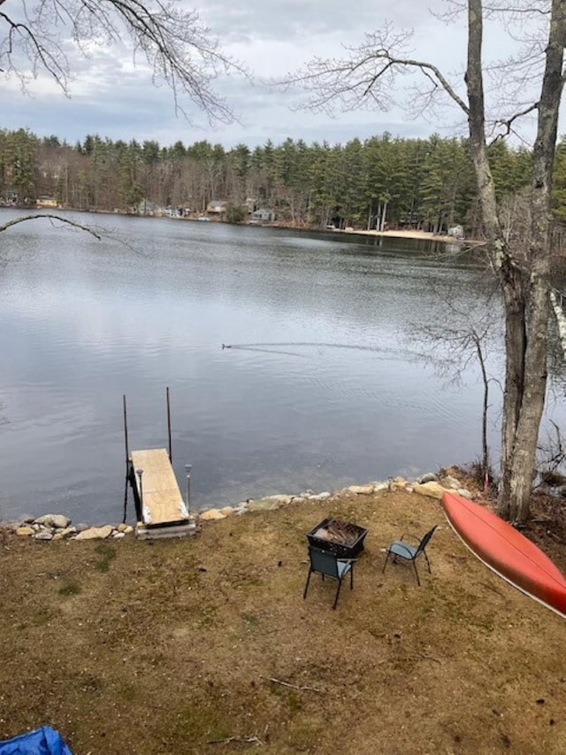 dock area with a water view, a wooded view, and an outdoor fire pit