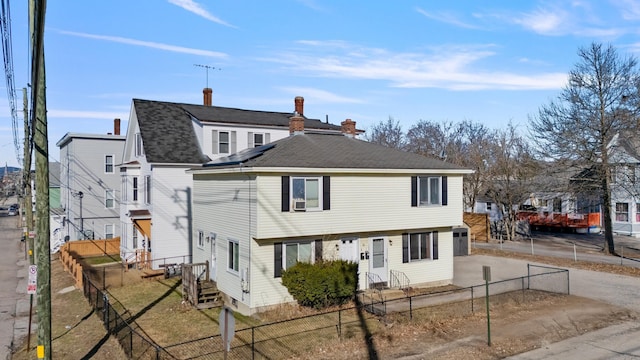 view of front facade featuring a fenced front yard, driveway, and a shingled roof