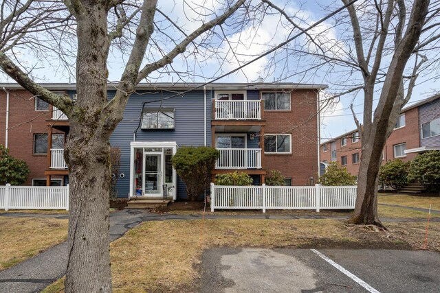 view of front facade with a balcony, fence, and brick siding