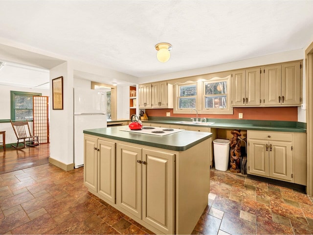 kitchen with dark countertops, a center island, stone tile flooring, white appliances, and a sink