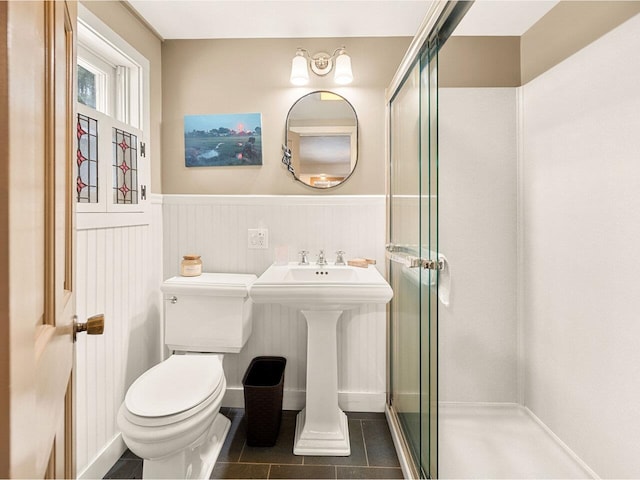 full bath featuring a wainscoted wall, toilet, a shower stall, and tile patterned flooring