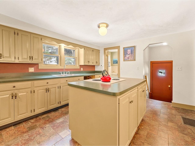 kitchen with visible vents, a sink, a kitchen island, stone tile floors, and white cooktop