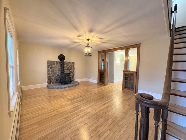 42 Elm St, Claremont, NH 03743 - unfurnished living room featuring stairs, a wood stove, wood-type flooring, baseboard heating, and baseboards