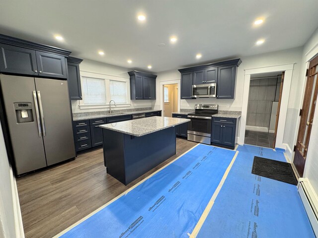 42 Elm St, Claremont, NH 03743 - kitchen featuring appliances with stainless steel finishes, a baseboard heating unit, a sink, a kitchen island, and light stone countertops