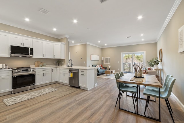 kitchen with light countertops, a sink, appliances with stainless steel finishes, a peninsula, and light wood-style floors