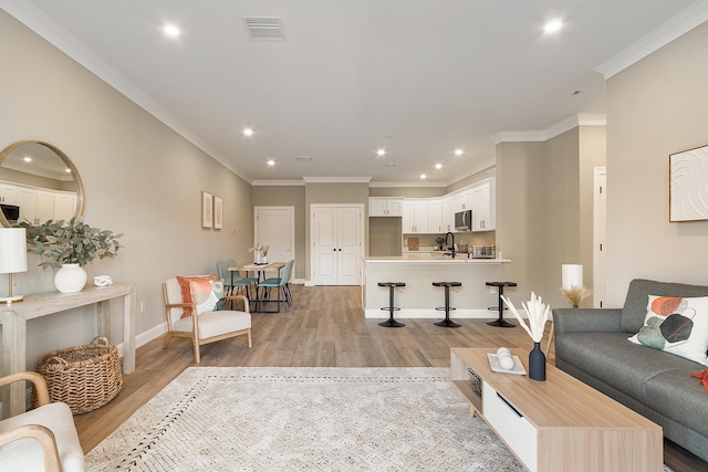 living area with visible vents, crown molding, light wood-style floors, and recessed lighting