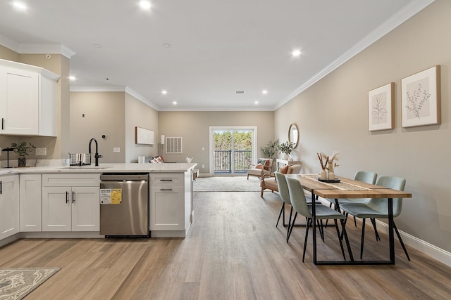 kitchen featuring stainless steel dishwasher, a sink, light wood finished floors, white cabinets, and a peninsula