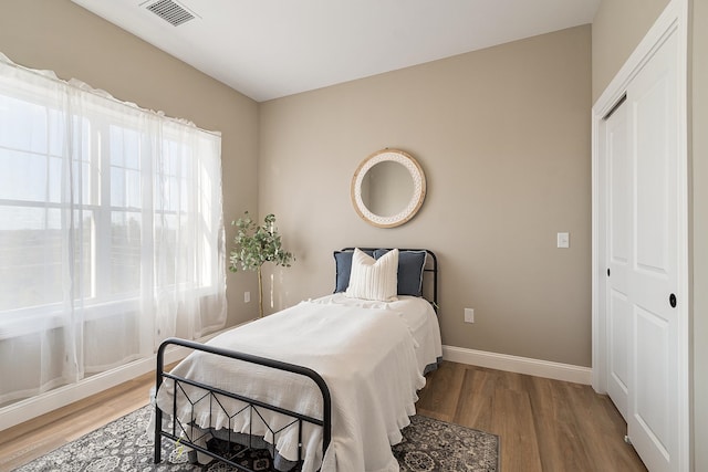 bedroom featuring wood finished floors, a closet, baseboards, and visible vents
