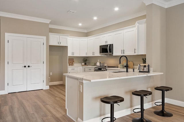 kitchen with a sink, a peninsula, stainless steel appliances, visible vents, and white cabinets