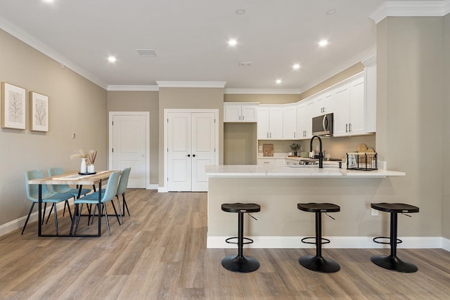 kitchen with white cabinets, light countertops, a peninsula, a breakfast bar, and stainless steel microwave