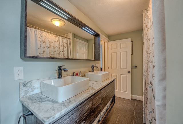 bathroom with baseboards, double vanity, and a sink