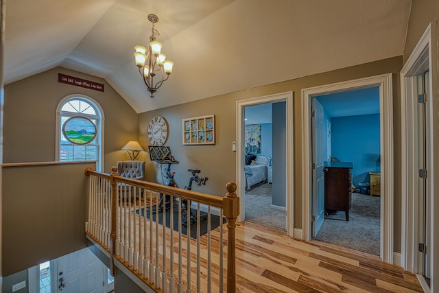 hall featuring a notable chandelier, an upstairs landing, vaulted ceiling, and wood finished floors