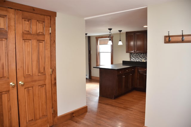 kitchen featuring light wood-type flooring, backsplash, dark countertops, a baseboard radiator, and a peninsula