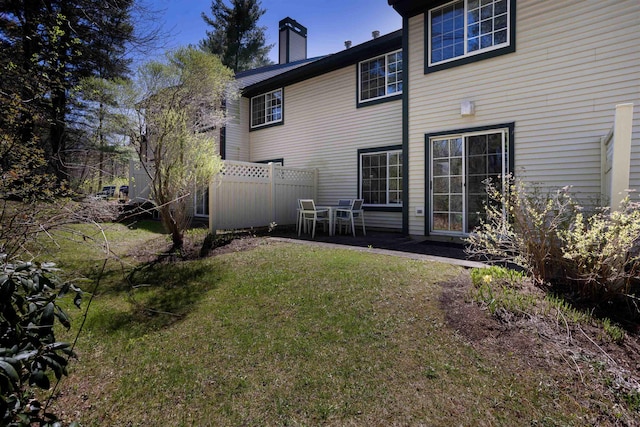 back of property with fence, a patio, a chimney, and a lawn