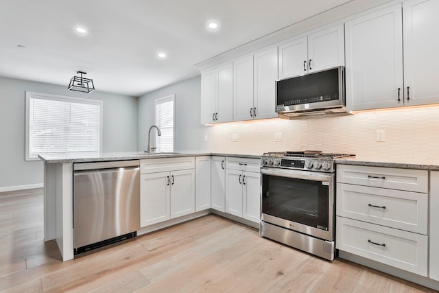 kitchen featuring a sink, backsplash, appliances with stainless steel finishes, a peninsula, and white cabinets