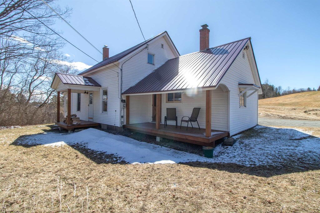back of property with a standing seam roof, metal roof, covered porch, and a chimney