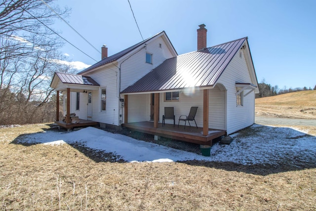 back of property with a standing seam roof, metal roof, covered porch, and a chimney