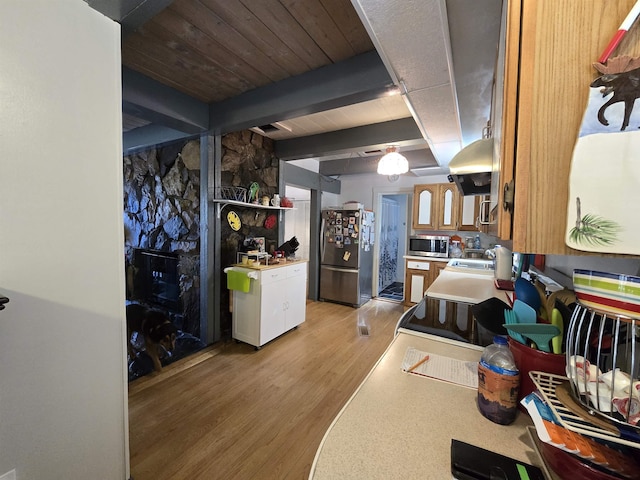 interior space with light wood finished floors, stainless steel appliances, a sink, beamed ceiling, and light countertops