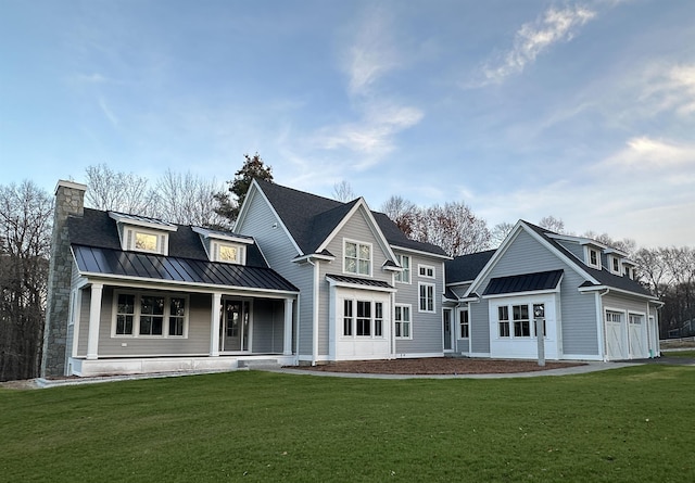rear view of property with a garage, covered porch, a standing seam roof, metal roof, and a lawn