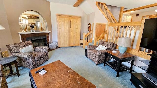 living room with stairway, carpet floors, arched walkways, a tiled fireplace, and vaulted ceiling with beams