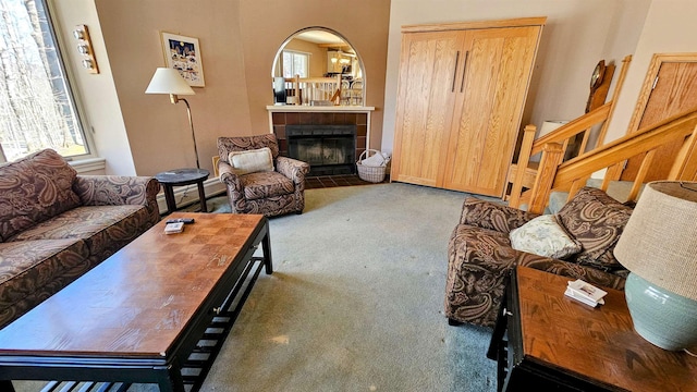 living area featuring arched walkways, a tile fireplace, stairway, and carpet