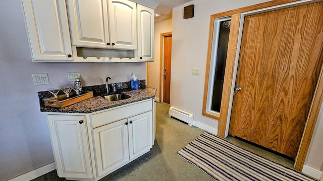 kitchen featuring white cabinets, a baseboard radiator, dark stone counters, dark carpet, and a sink