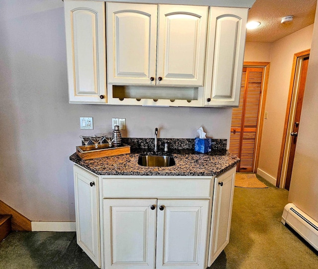 kitchen featuring baseboards, dark stone countertops, a baseboard heating unit, and a sink