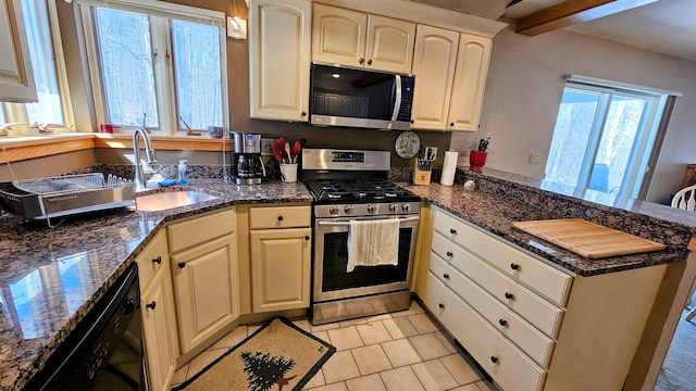 kitchen featuring a sink, appliances with stainless steel finishes, a peninsula, dark stone countertops, and light tile patterned floors