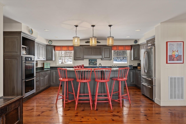 444 Tin Shanty Rd, Shrewsbury, VT 05738 - kitchen with dark wood-style flooring, stainless steel appliances, a breakfast bar, an island with sink, and visible vents