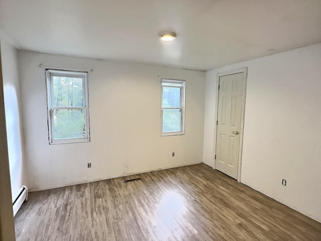 unfurnished room with a wealth of natural light, baseboard heating, visible vents, and wood finished floors